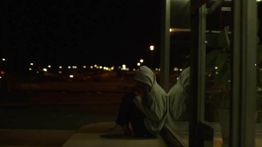 A woman leans against a glass wall and curls up