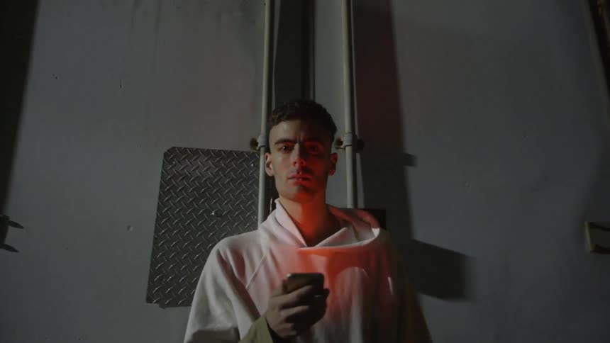 Man in a white sweatshirt holds a cell phone at night