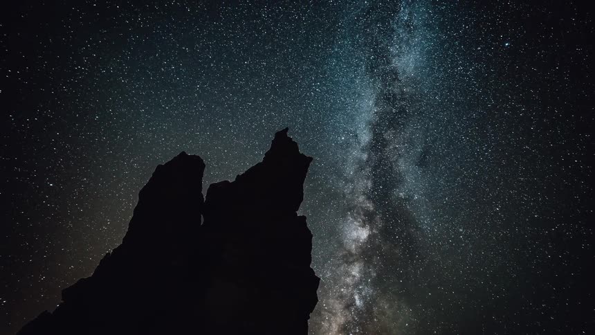 The milky way and stars are moving in the night sky above a rock pillar