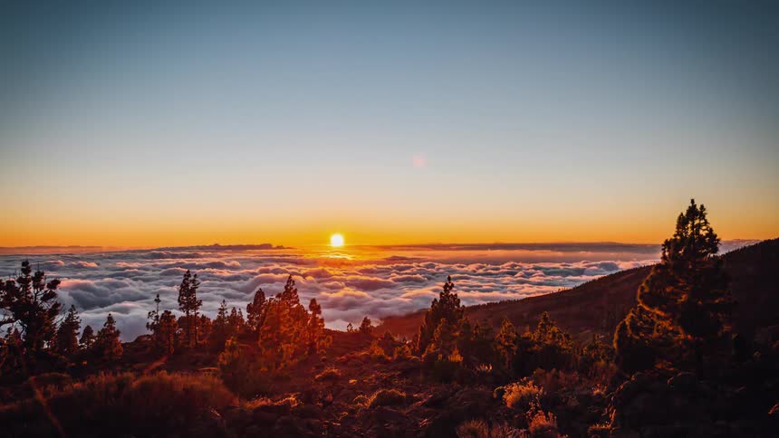 The sun sets on the horizon over rolling clouds