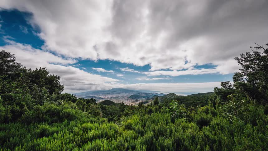 Clouds billow and roll over a mountain landscape during the day