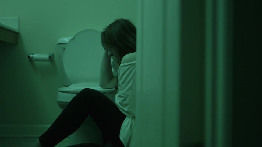 A woman sits on the ground next to a toilet