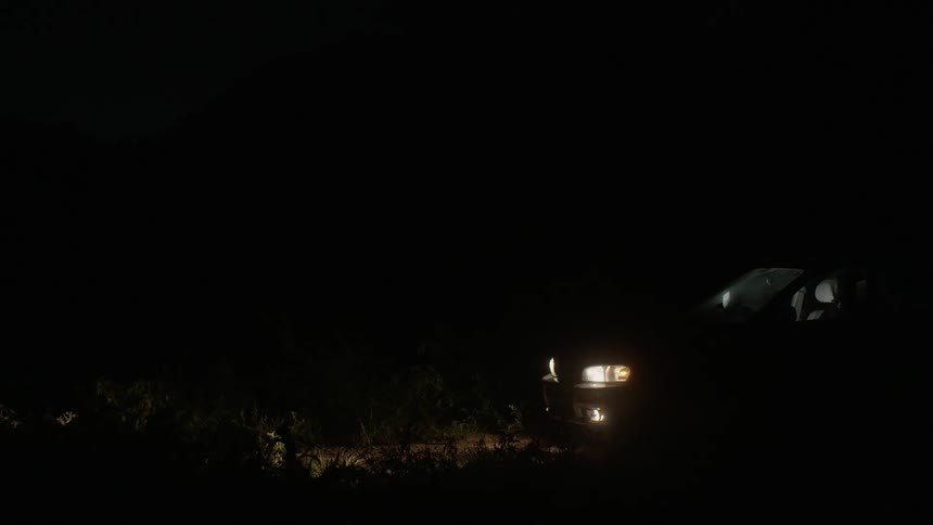 A car sits parked with its headlights on at night