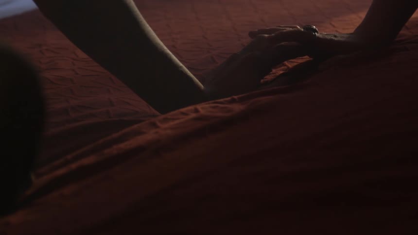 Two people are sitting on a bed touching each others hands