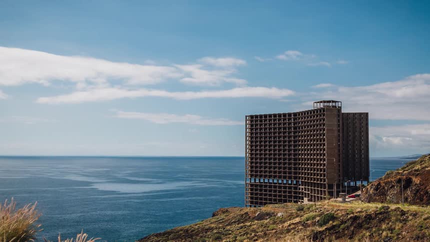 Clouds pass over an unfinished building in a coastal area during the day