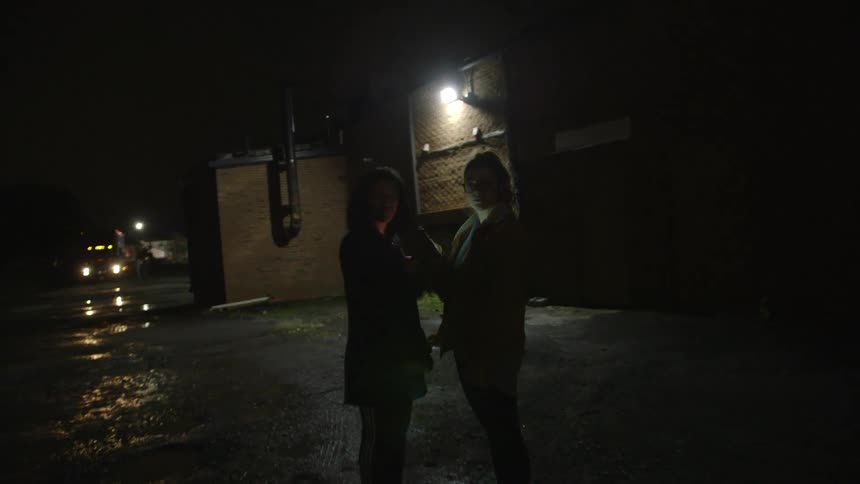 Two women stand in a parking lot holding flashing phones