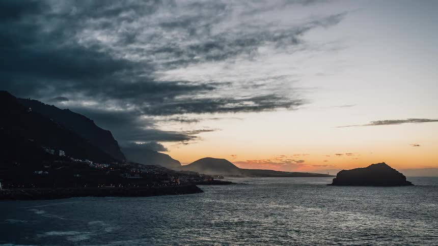 The sun is setting beyond a city on a rocky coastline