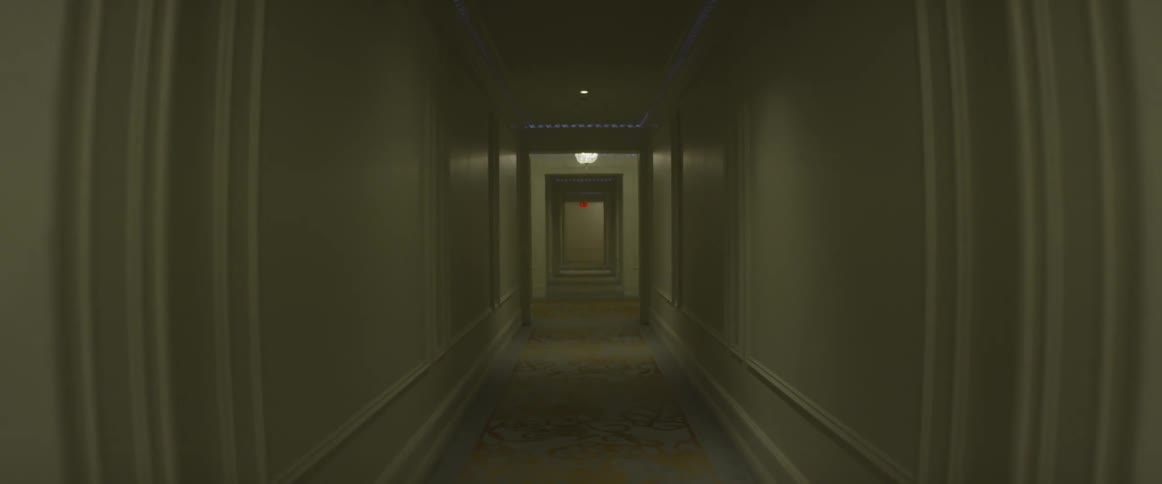An exit sign glows at the end of a hotel hallway