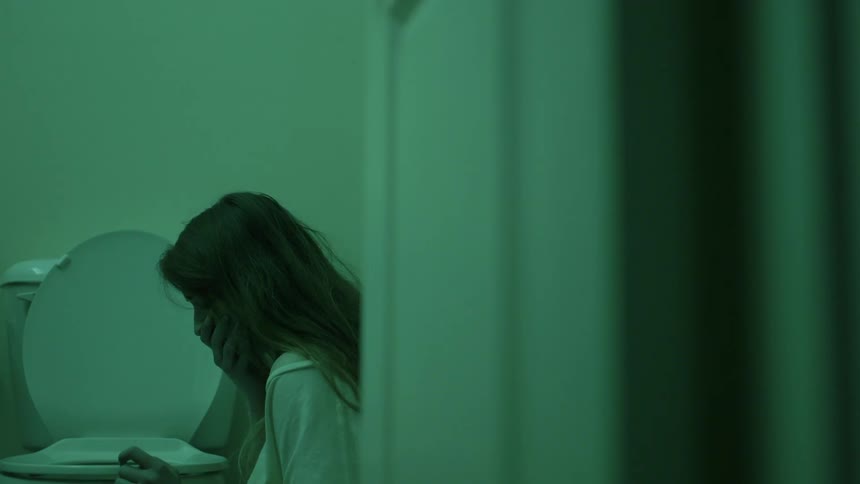 A woman sitting on a bathroom floor covers her mouth