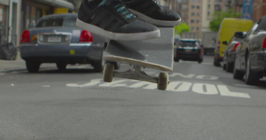 A skateboarder is flipping his board as he rides in an urban street