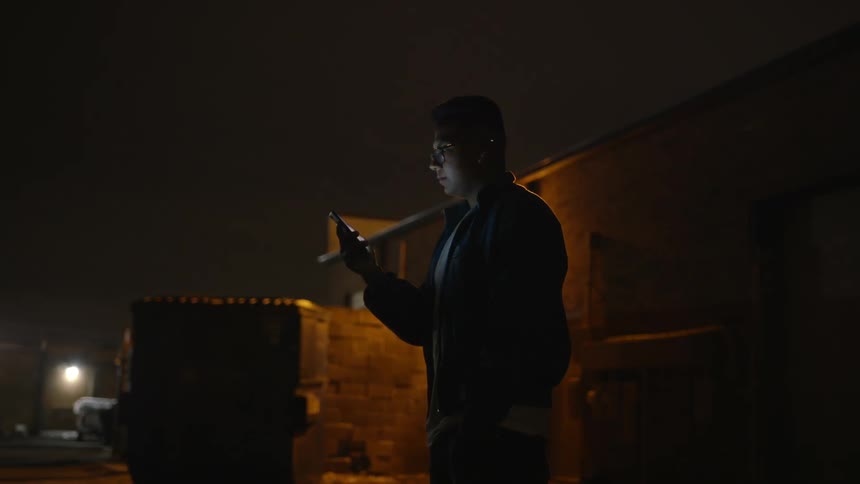 A man is standing outside at night watching something on his cellphone