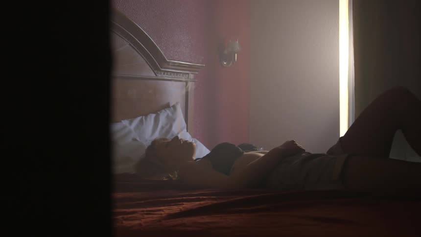 A woman is lying on a bed smoking during the day