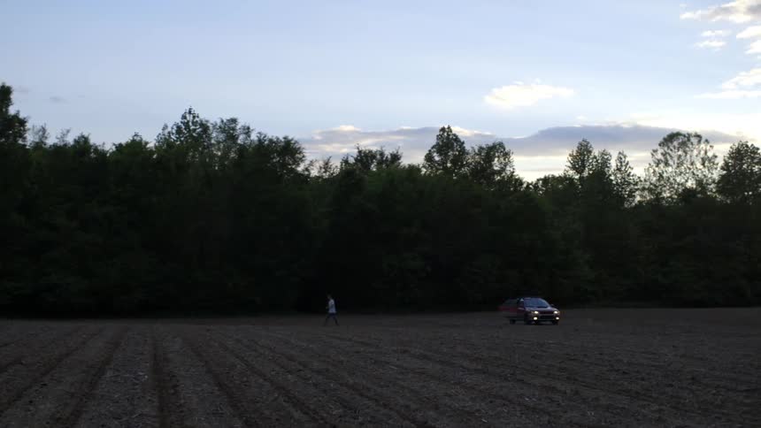Person walking away from a parked car in a large field