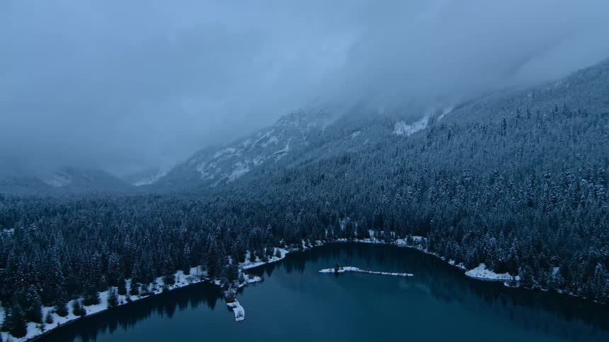 A snow covered forest and lake is being filmed from a drone