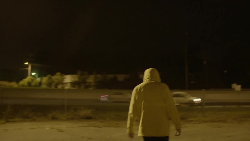 A person in a yellow jacket walks toward the road
