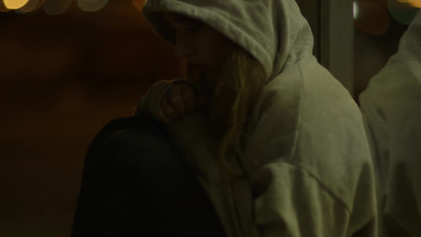 A girl is sitting on the ground outside with a hoodie on