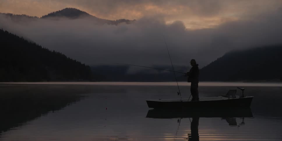 A fisherman is standing on his boat in the middle of a lake