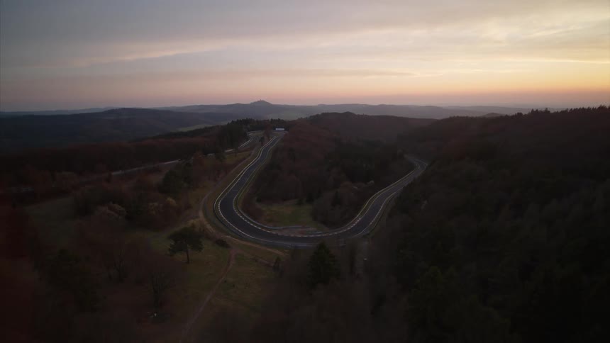 A winding road is being filmed by a drone at sunset