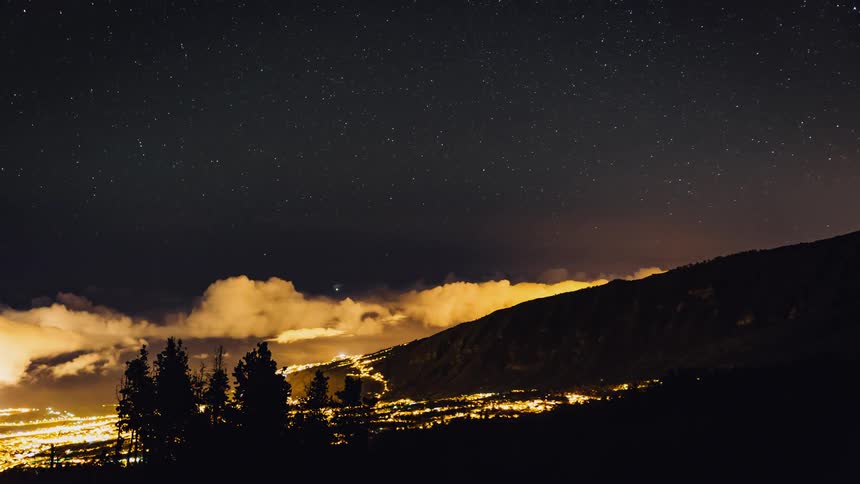 Clouds roll into and recede from a city in a valley at night