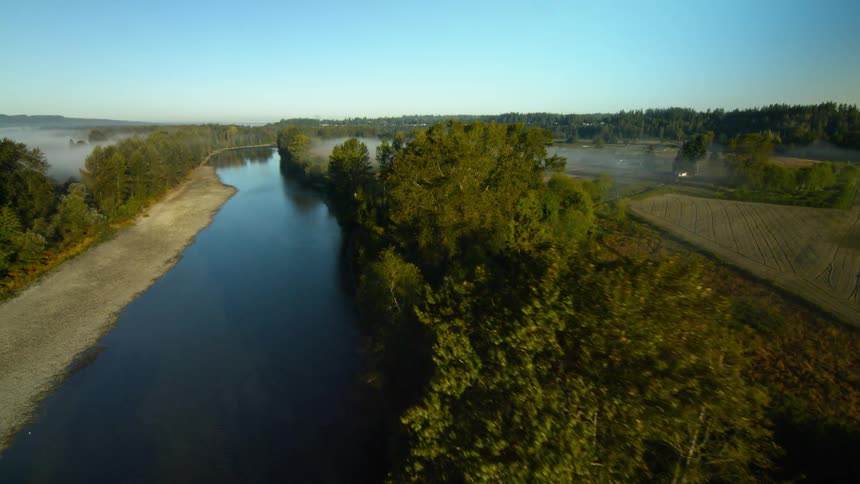 A drone films a small river and foggy fields