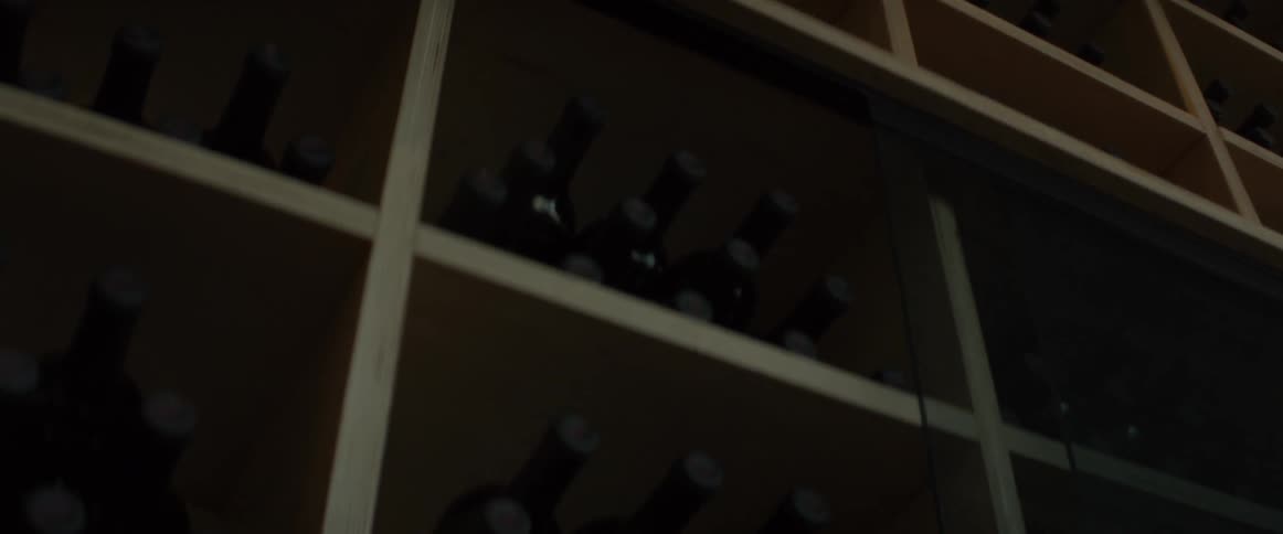 Wine bottles are stacked on a wall of open shelves