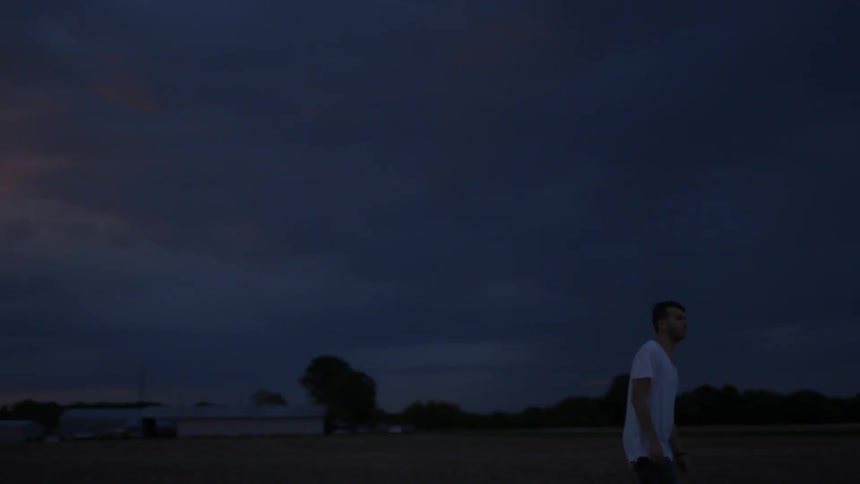 A man is walking through an empty field at dusk