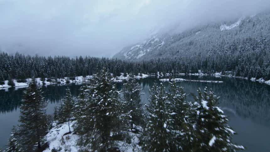Fog and clouds hover over a mountain lake in a snow-covered landscape