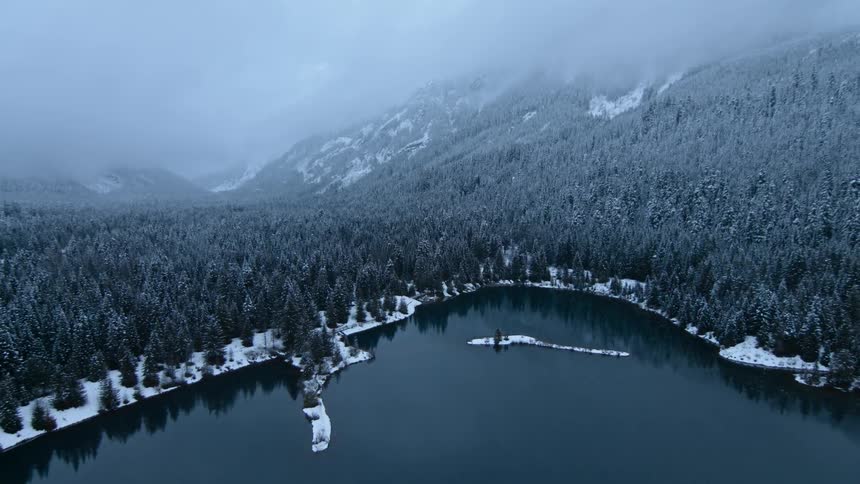 A calm mountain lake is surrounded by trees and snow