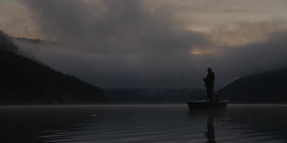 A man stands in a boat fishing at dusk or dawn