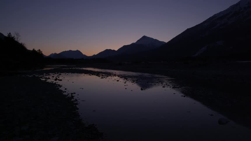 A river's surface reflects the sky and mountains at sunset