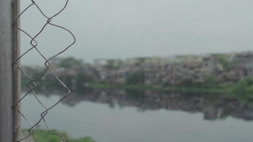 A broken fence stands before a river and a shanty town