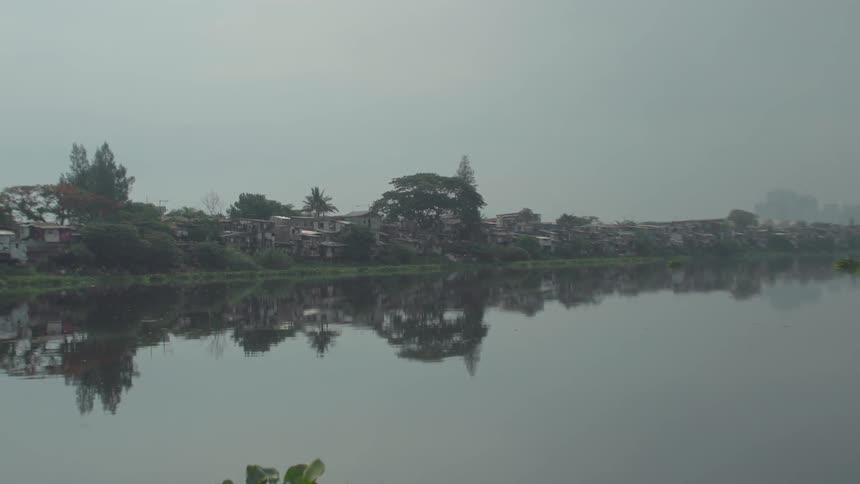 Buildings and trees are reflected in a river on a hazy day