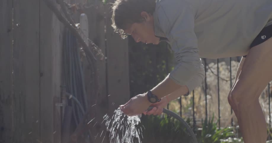 A man drinks water from a hose during the day