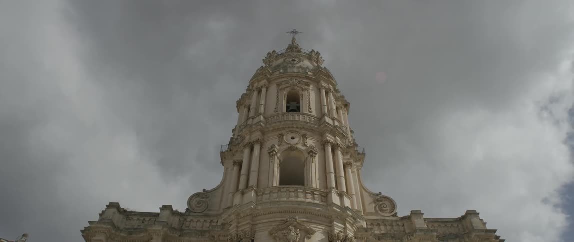 A tall stone building has a cross at the top