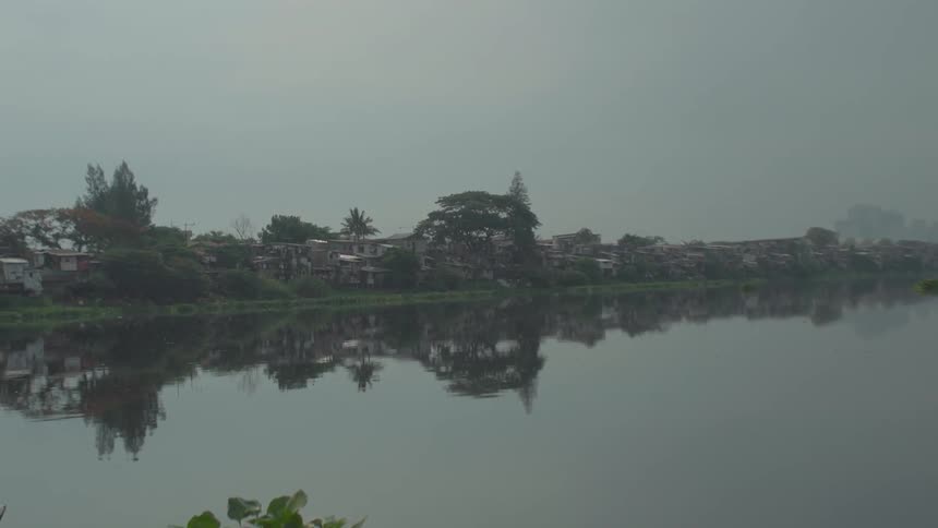 Haze hangs over a shanty town on a river during the day