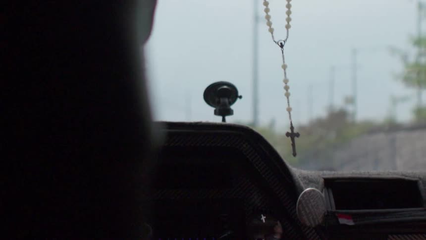 A rosary sways on the rearview mirror of a car