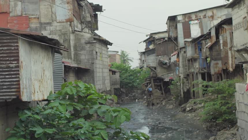 A muddy stream flows through a shanty town during the day