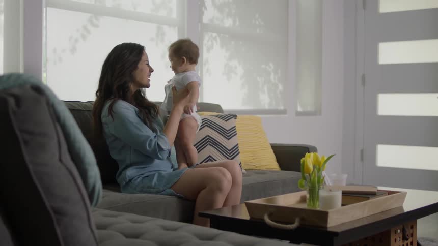 A woman is sitting on a couch playing with a baby