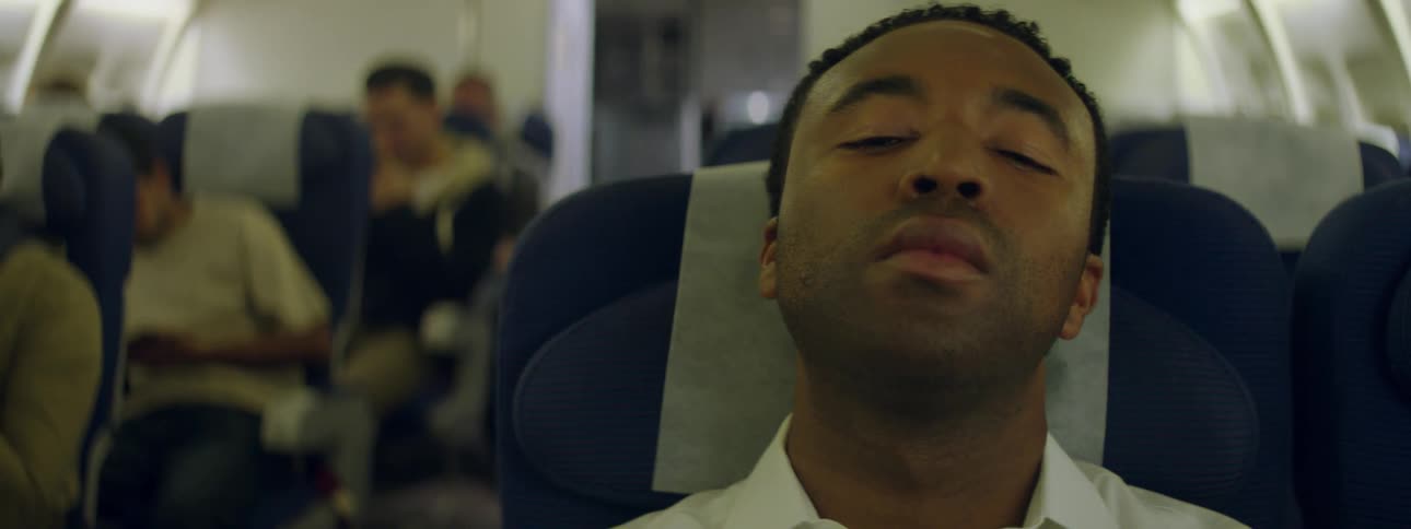 A man sitting in an airplane is looking up at the ceiling and fidgeting