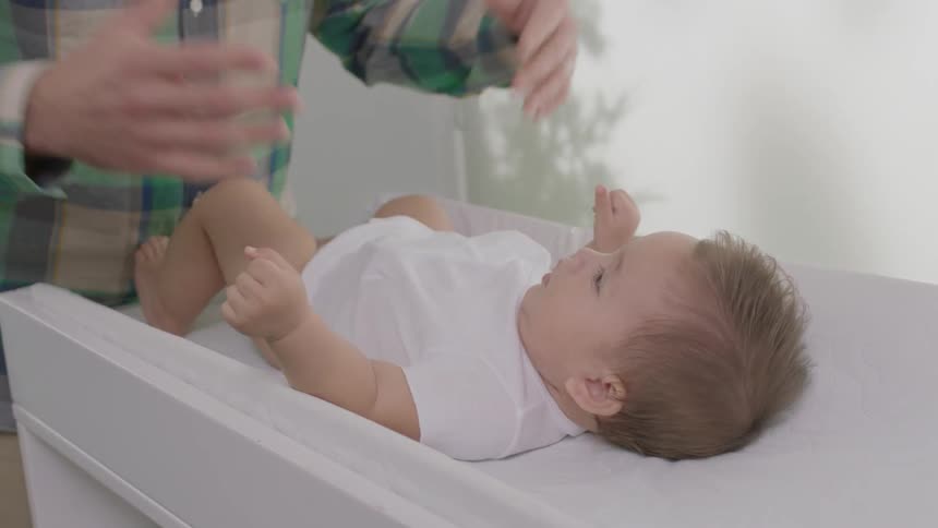 A man fastens a onesie on a baby