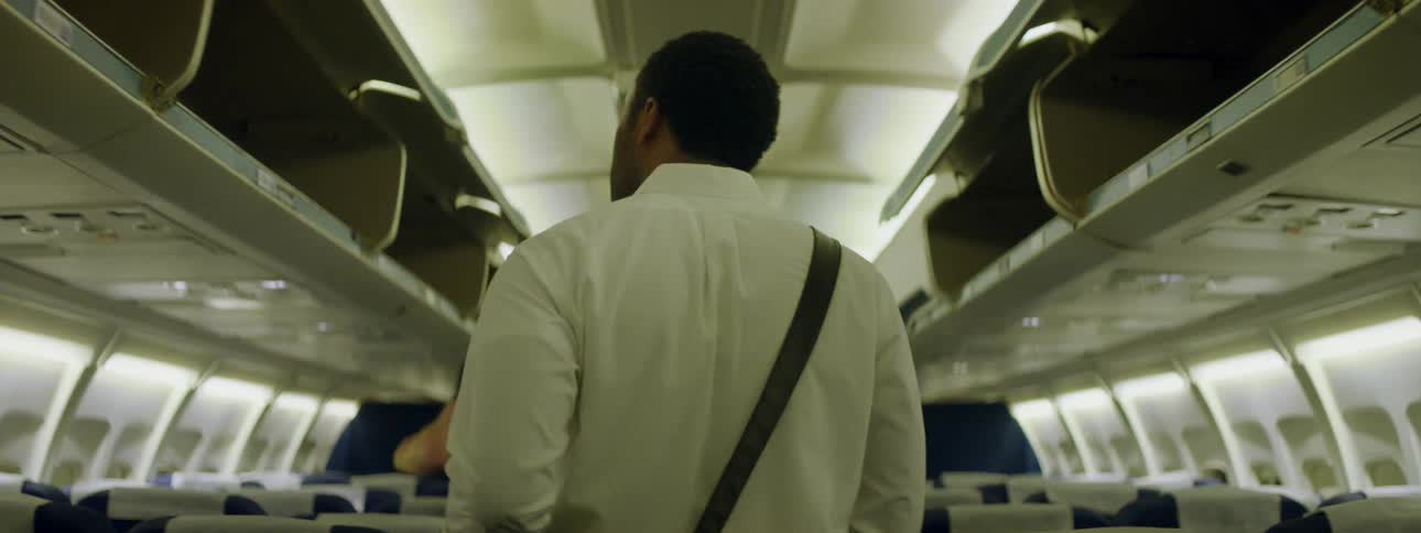 Man walks down the aisle of an airplane and sits down