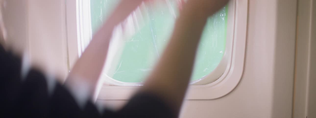 A woman closes the screen on an airplane window