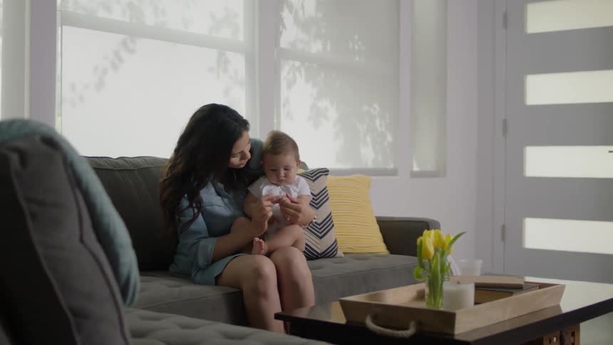 Woman and baby sit on a couch in front of a window