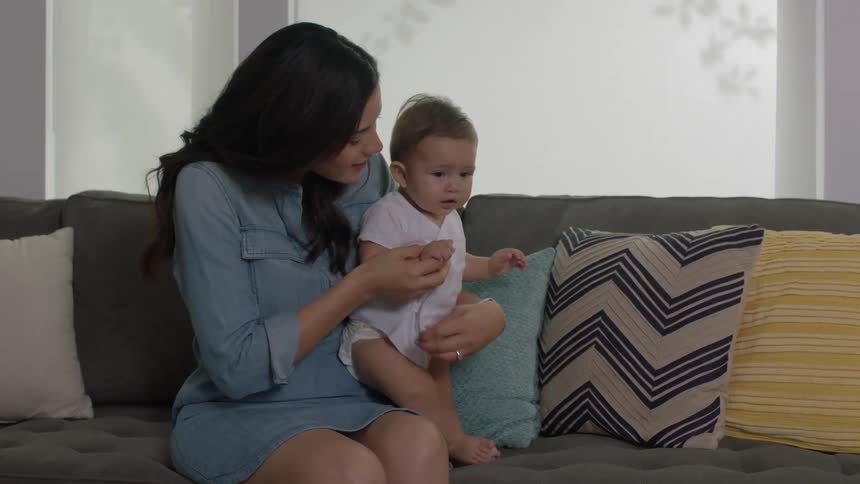 Woman holds a baby on her lap as she sits on a sofa