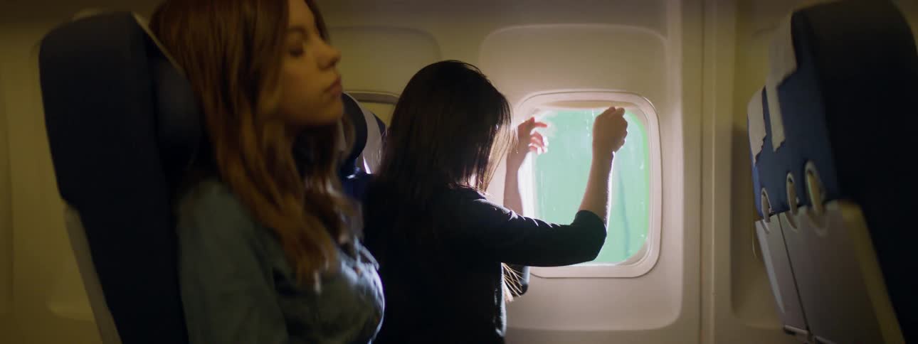 A woman lifts the screen on an airplane window and looks out