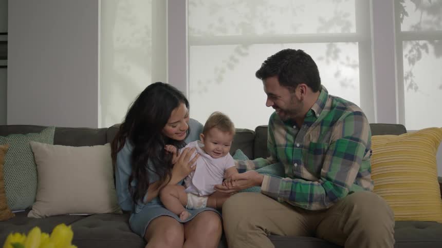 A couple sit on a couch holding and playing with a baby