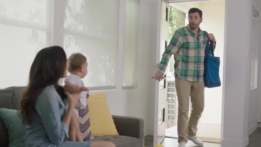 A woman bounces a baby on her lap as a man enters the house door