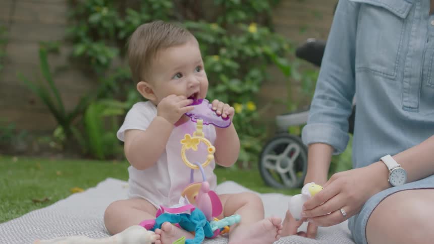 A baby sits on a blanket chewing on a teething toy