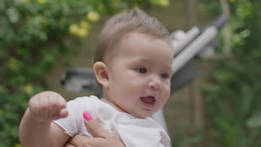 A baby laughs as a woman holds it as they play outside