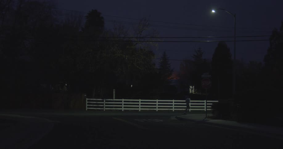 A man jogs past a white fence at night